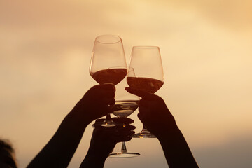 Fototapeta na wymiar Friends clinking glasses with wine and enjoying wine against a beautiful sunset.