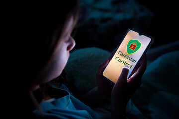 A child using smart phone lying in bed late at night, playing games. Children's screen addiction and parent control concept. Child's room at night. Parental control lock on screen