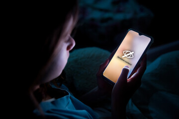 Fototapeta A child using smart phone lying in bed late at night, playing games. Children's screen addiction and parent control concept. Child's room at night. Sensitive content on screen obraz