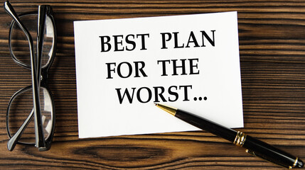 BEST PLAN FOR THE WORST - words on a white sheet on a brown wooden background with a pen and glasses