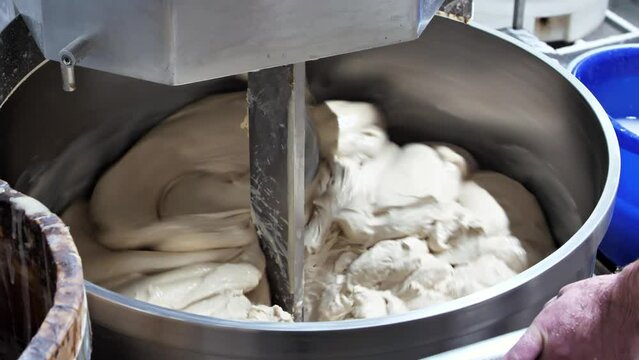 Baker knead the dough for bread in a dough mixer in an industrial bakery. Production of bakery products.