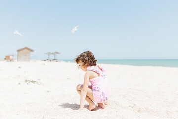 Naklejka premium happy child girl wearing swimsuit sitting on beach in the day time. Lifestyle photography. Pastel colors