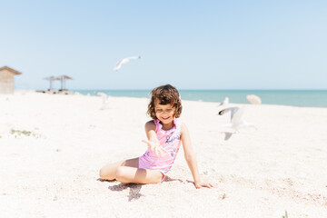 happy child girl wearing swimsuit sitting on beach in the day time. Lifestyle photography. Pastel colors