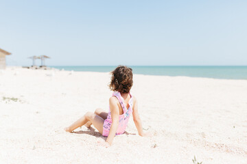 happy child girl wearing swimsuit sitting on beach in the day time. Lifestyle photography. Pastel colors