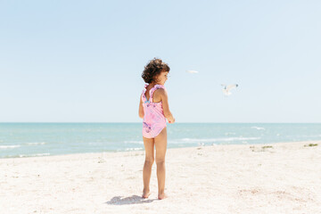 Fototapeta na wymiar happy child girl wearing swimsuit feeding seagulls on beach day time. Lifestyle photography. Pastel colors