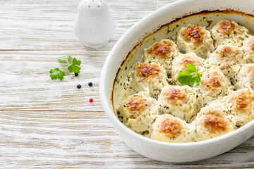 Rustic cream parmesan meatballs in baking dish on wooden background. Top view, copy space, flat lay.