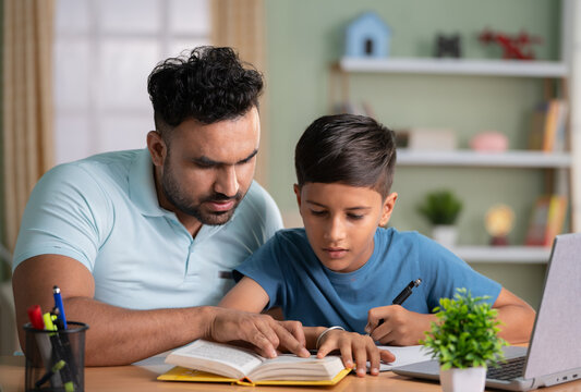 Indian father teaching or helping the son for reading from book at home - concept of Parental Guidance, home education and Tutoring Sessions.