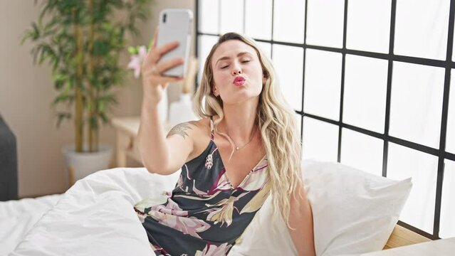 Young blonde woman make selfie by smartphone sitting on bed at bedroom