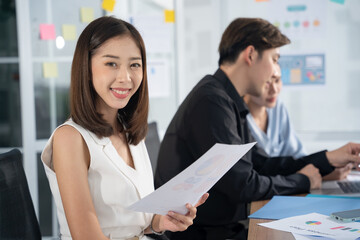 Attractive asian young confident businesswoman sitting at the office table with group of colleagues in the background. Business woman with coworkers in meeting room.
