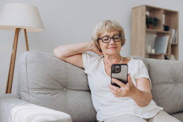 Senior woman with mobile phone on her hands sitting in room and sending messages to her friends and family. Senior woman typing on her mobile phone