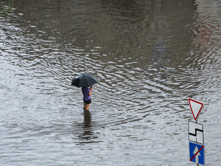 Kyiv, Ukraine - July 7, 2023: A man under umbrella stands in the middle of a flooded intersection and takes pictures