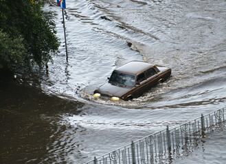 Kyiv, Ukraine - July 7, 2023: A brown car passes through a flooded road area after heavy rain