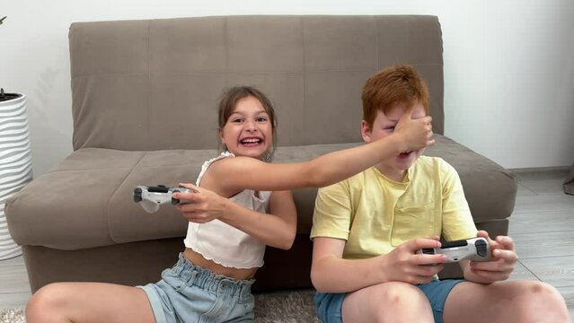 two children play video games, a brother and sister play computer games, hold joysticks in their hands, the concept of a family vacation of real people, a boy and a girl play at home