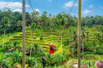 Young female tourist in red dress enjoying the Bali swing at tegalalang rice terrace in Bali, Indonesia - obrazy, fototapety, plakaty