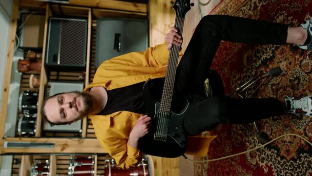 portrait of young smiling rock artist with electric guitar in recording studio playing own track on musical instrument drums vertical video