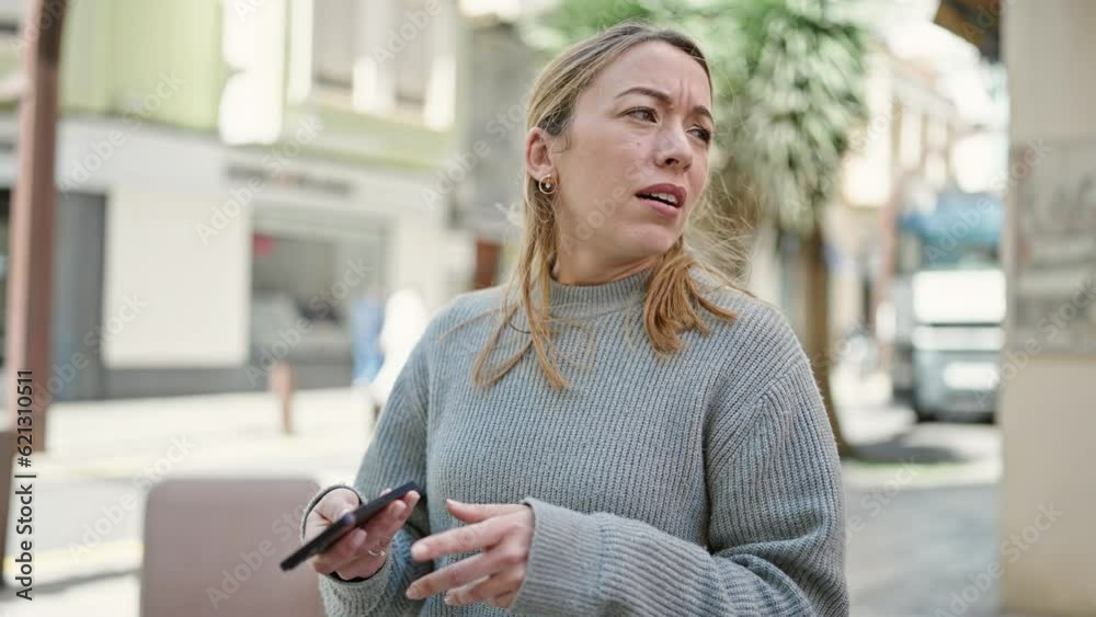 Poster Young blonde woman using smartphone with serious expression at street