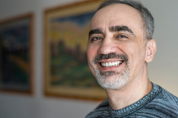 Adult middle aged man smiling with teeth. He is wearing a casual sweater. Happy face with gray beard and thick eyebrows. Chest-length portrait of caucasian person.