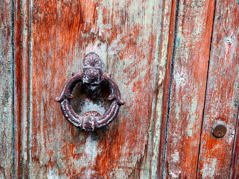 Old door knocker on an old wooden door with peeling paint