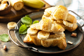 Healthy food dessert concept. French pastry. Tasty freshly baked croissants with peanut butter and banana on a rustic background.
