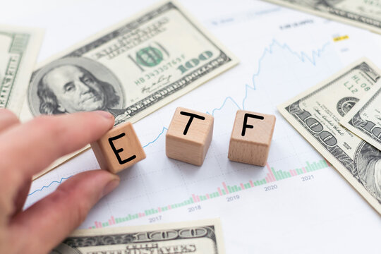 Wooden cubes with blue letters forming the word ETFS (Exchange Traded Funds) on dollar bills on a table. Investment concept photo. 