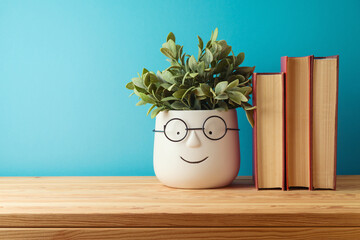 Back to school concept with books and cute funny plant on wooden table over blue background