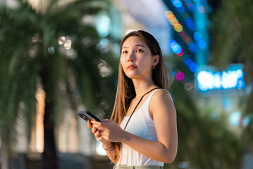 Asian woman using a smartphone standing against Bangkok city walking street at night