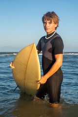 Teenage surfer boy in wet suit standing in the water while holding his surfboard