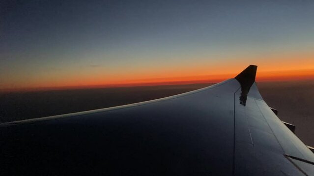 The view from an airplane window over the wing to a beautiful orange and blue sunset in the evening.