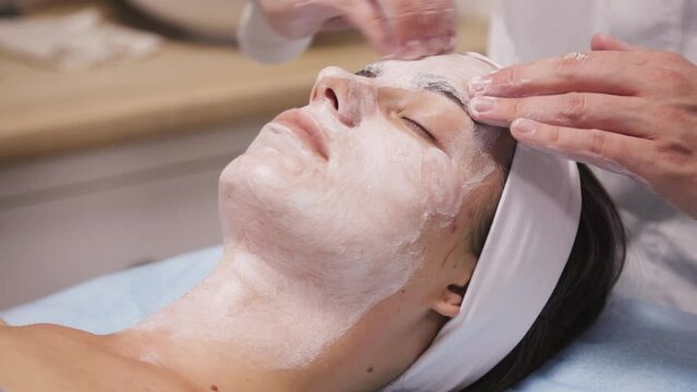 Cosmetologist applies a nourishing mask to a young woman in a spa salon.