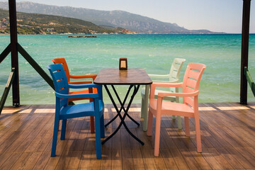 Empty table with four colorful chairs, on the pier above the turquoise sea