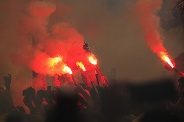 Red Colored smoke dye being grabbed by people in a stadium: Supporters crowd celebrating with fire...
