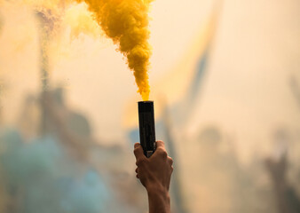 Yellow colored smoke dye being grabbed by a hand in a stadium with out of focus and blurred people...