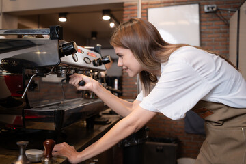 Young female barista preparing coffee in cafe. Female barista using coffee machine.