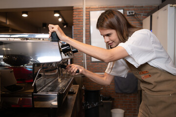 Young female barista preparing coffee in cafe. Female barista using coffee machine.