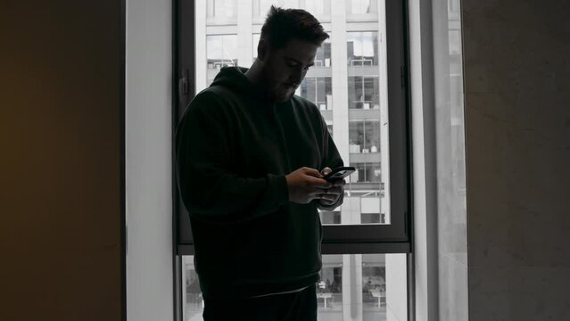 a man with a phone in his hands solves business issues on the background of a window with a view of the business center