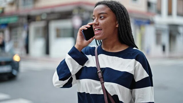 African american woman talking on the smartphone looking watch at street
