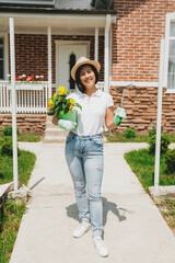 A gardener woman stands with a flower near her house. A woman in an apron takes care of flowers in the garden.