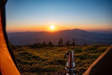 Device for making coffee - a moka pot on a gas burner in front of a tent on a mountain peak in the Polish mountains - Beskidy. Sunrise at a mountain campsite.