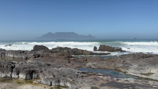 waves and beach and rocks with Table Mountain in cape Town in the background