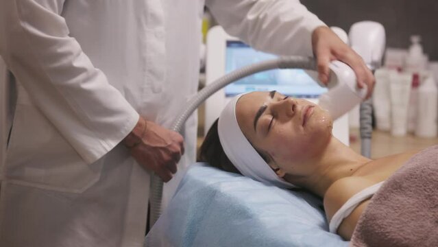Microneedle RF lifting procedure. Hardware cosmetology. Beautician conducts a facial rejuvenation procedure for a brunette woman