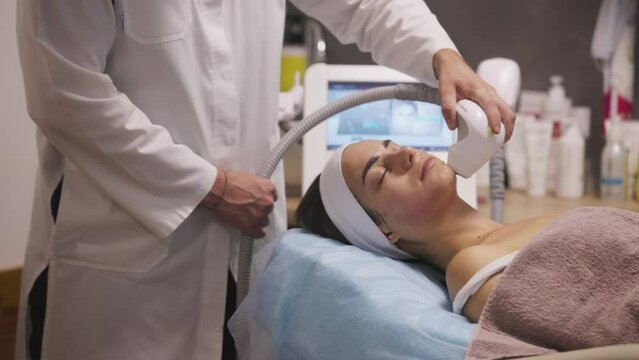 Microneedle RF lifting procedure. Hardware cosmetology. Beautician conducts a facial rejuvenation procedure for a brunette woman