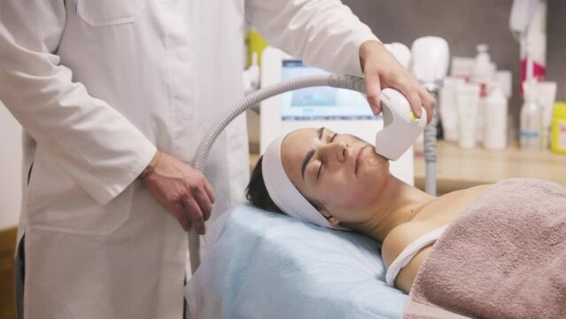Microneedle RF lifting procedure. Hardware cosmetology. Beautician conducts a facial rejuvenation procedure for a brunette woman