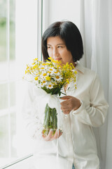 portrait of an asian woman with a bouquet of wild flowers at home near the window.