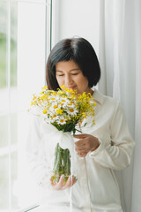 portrait of an asian woman with a bouquet of wild flowers at home near the window.