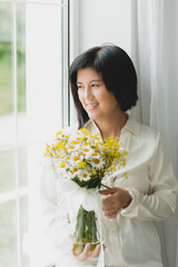 portrait of an asian woman with a bouquet of wild flowers at home near the window.