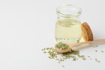 Aroma oil  in glass container witht green fennel seeds in wooden spoon isolated with copy space