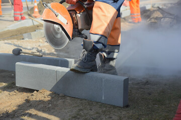 A builder with a saw in his hands is going to cut a concrete block, repairs a road for pedestrians.