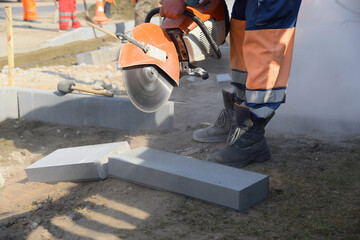 A worker saws a large concrete block with a circular saw on a construction site.