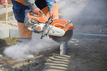 A worker saws a concrete block with a circular saw, road construction.