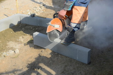 A builder saws a concrete block with a circular saw, repairs a road for pedestrians.